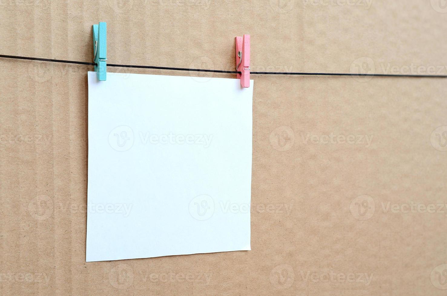 White blank card on rope on a brown cardboard background. Creative reminder, small sheet of paper on wooden clothespin, memo backdrop photo