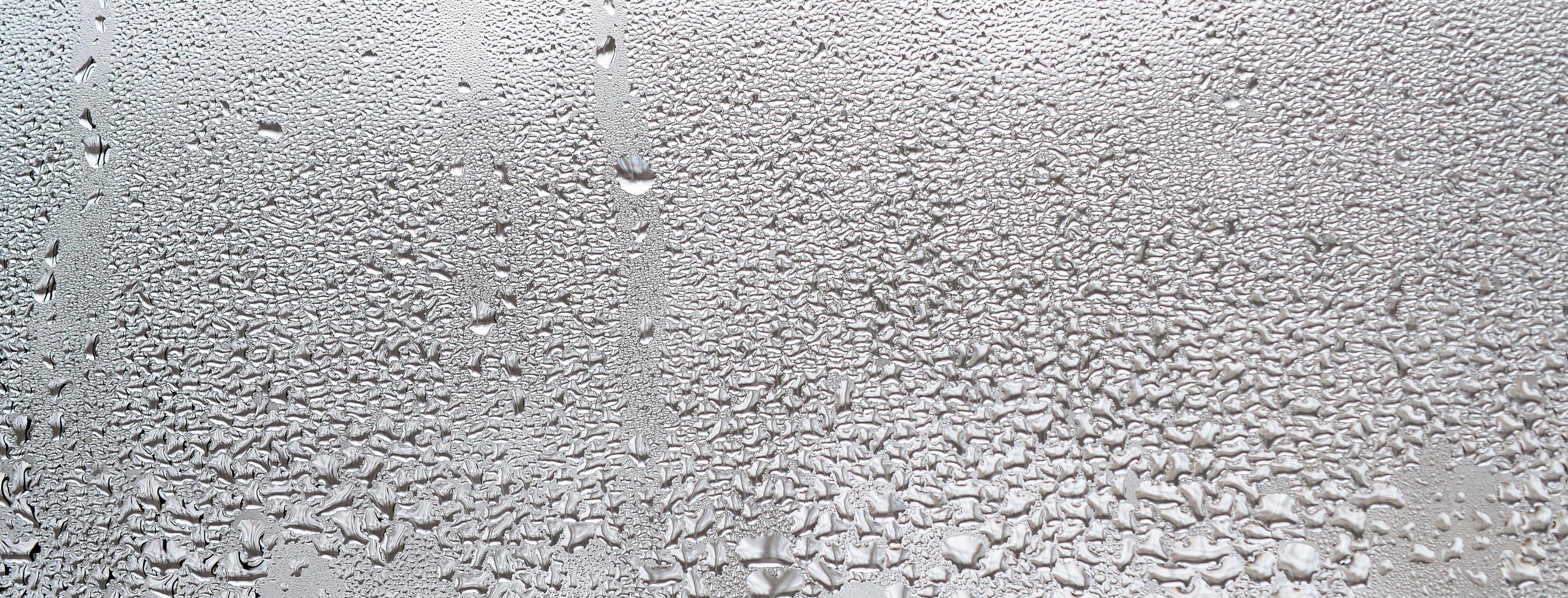 textura de una gota de lluvia sobre un fondo transparente húmedo de vidrio. tonificado en color gris foto