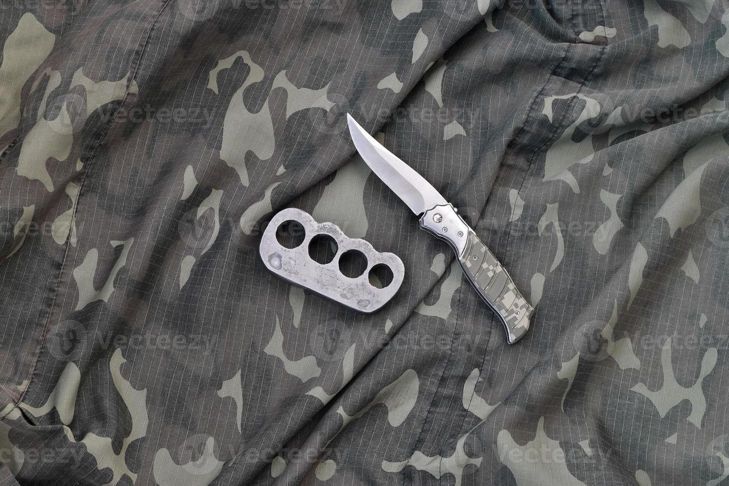 cuchillo y nudillos de latón sobre un fondo de ropa de camuflaje. herramientas para la autodefensa o ataques de delincuentes foto