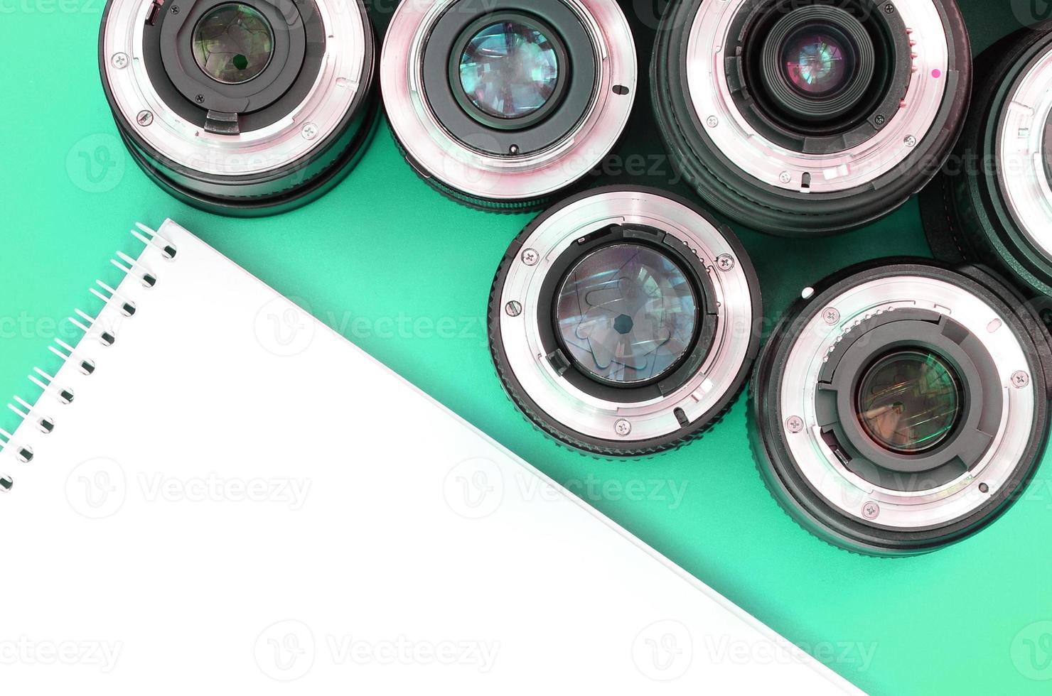 Several photographic lenses and white notebook lie on a bright turquoise background. Copy space photo