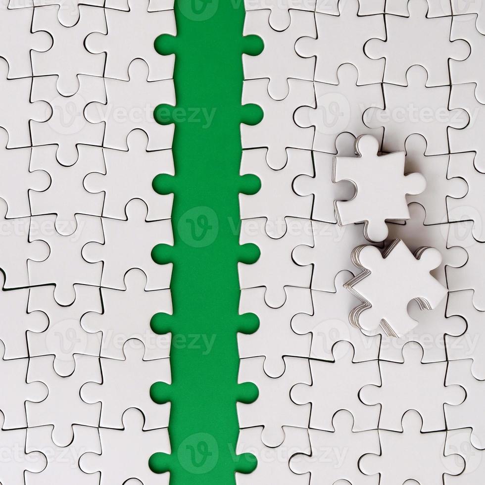 The green path is laid on the platform of a white folded jigsaw puzzle. The missing elements of the puzzle are stacked nearby. Texture image with space for text photo