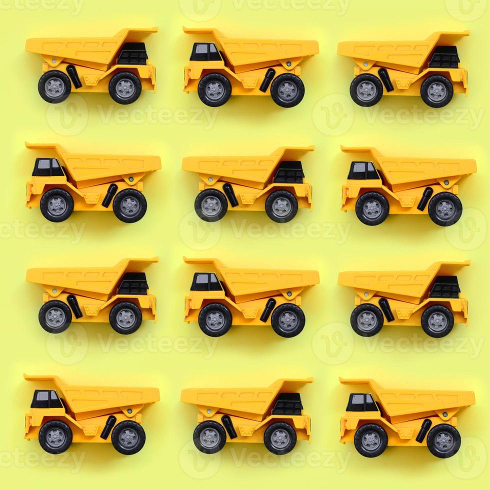 Many small yellow toy trucks on texture background of fashion pastel yellow color paper in minimal concept photo