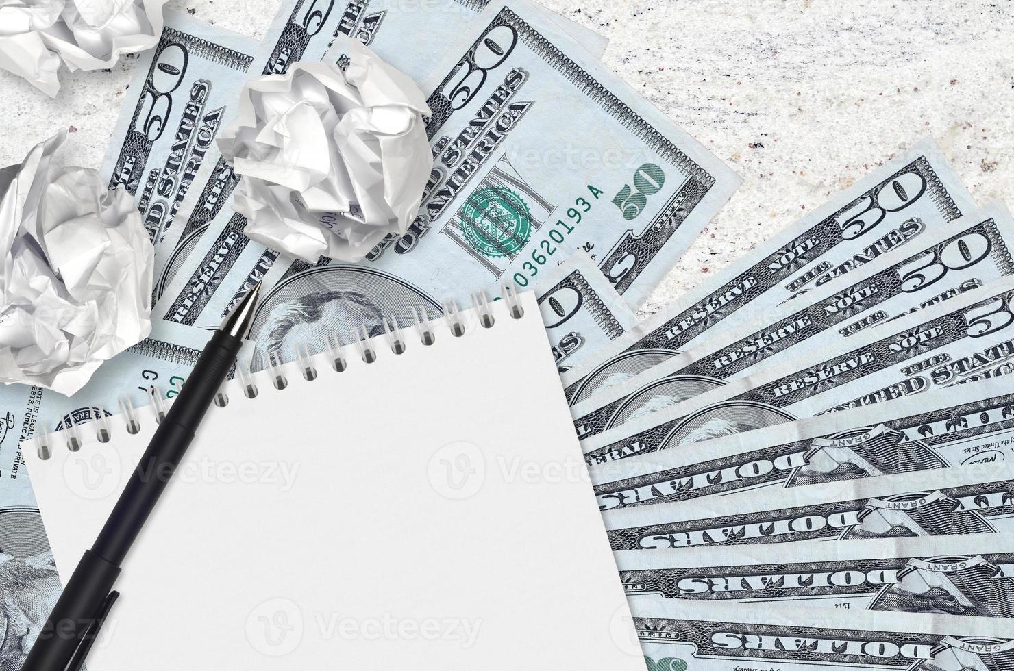 50 US dollars bills and balls of crumpled paper with blank notepad. Bad ideas or less of inspiration concept. Searching ideas for investment photo