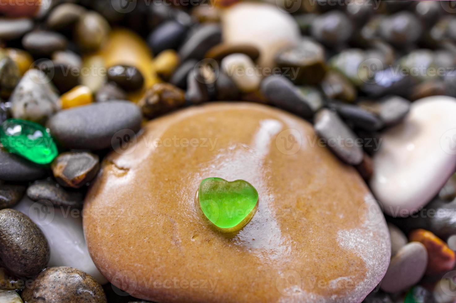 Pebble stone background with small green transparent heart shaped pebble. Abstract photo