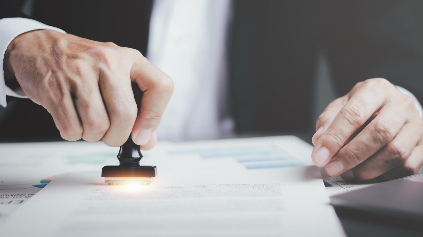 A young executive is stamping on documents for a business contract. Transaction and document management concepts include negotiating corporate entities and filling out legal forms or agreements. photo