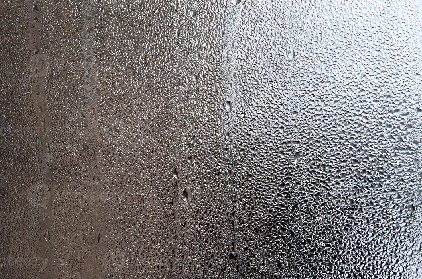 textura de una gota de lluvia sobre un fondo transparente húmedo de vidrio. tonificado en color gris foto