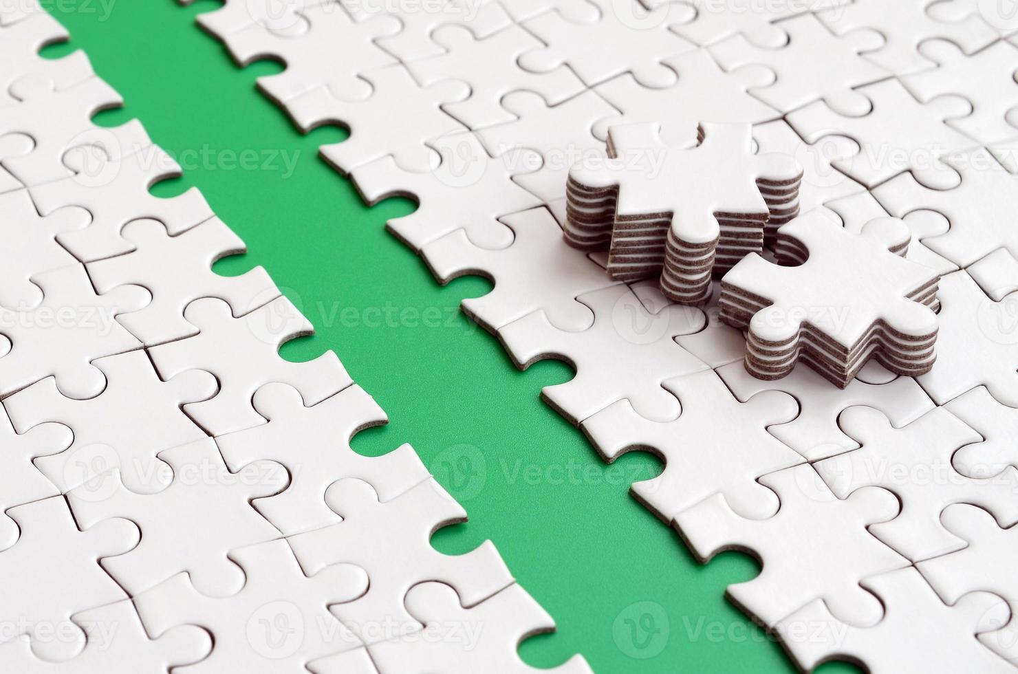 The green path is laid on the platform of a white folded jigsaw puzzle. The missing elements of the puzzle are stacked nearby. Texture image with space for text photo