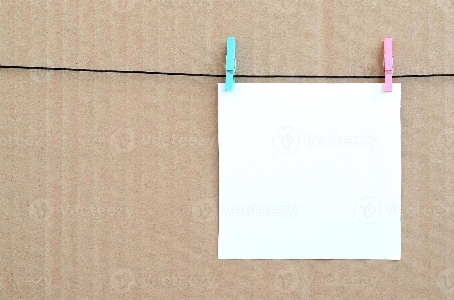 tarjeta blanca en blanco sobre una cuerda sobre un fondo de cartón marrón. recordatorio creativo, hoja pequeña de papel sobre pinza de madera, telón de fondo de memo foto