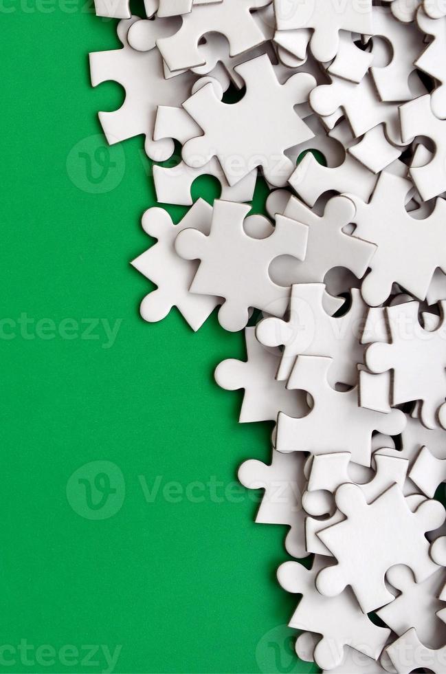 A pile of uncombed elements of a white jigsaw puzzle lies on the background of a green surface. Texture photo with copy space for text