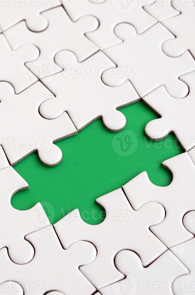 Close-up texture of a white jigsaw puzzle in assembled state with missing elements forming a green pad for text. Copy space photo