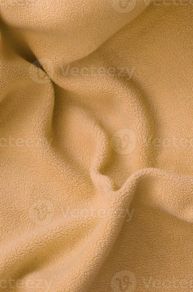 The blanket of furry orange fleece fabric. A background of light orange soft plush fleece material with a lot of relief folds photo