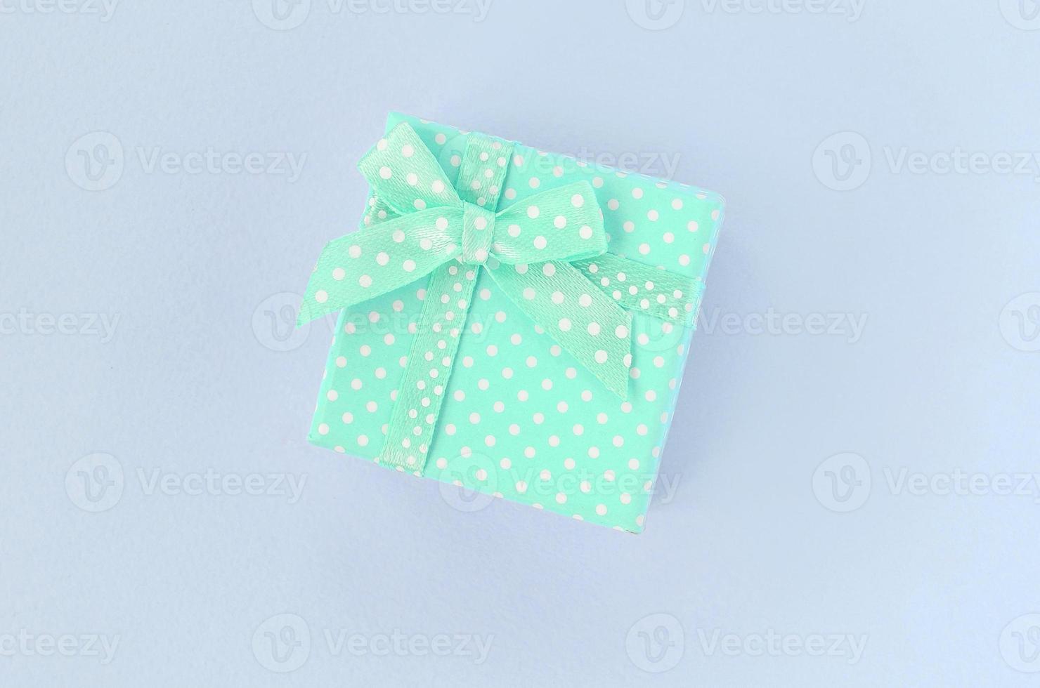 Small blue gift box with ribbon lies on a violet background photo