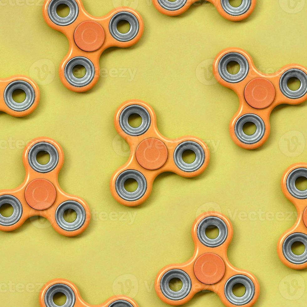 Many orange fidget spinners lies on texture background of fashion pastel orange color paper photo