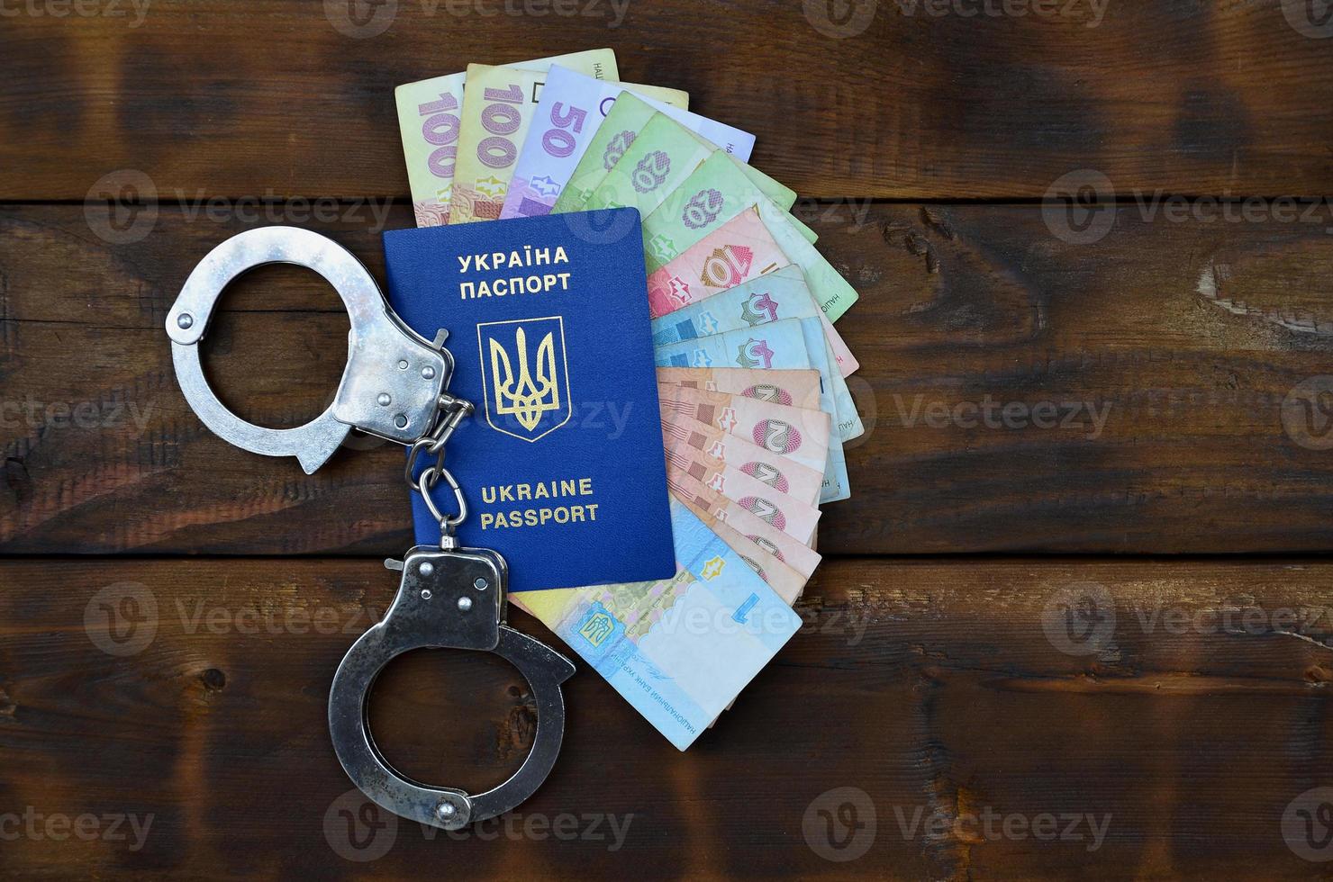 A photograph of a Ukrainian foreign passport, a certain amount of Ukrainian money and police handcuffs. Concept of illegal earnings of Ukrainian citizens abroad photo