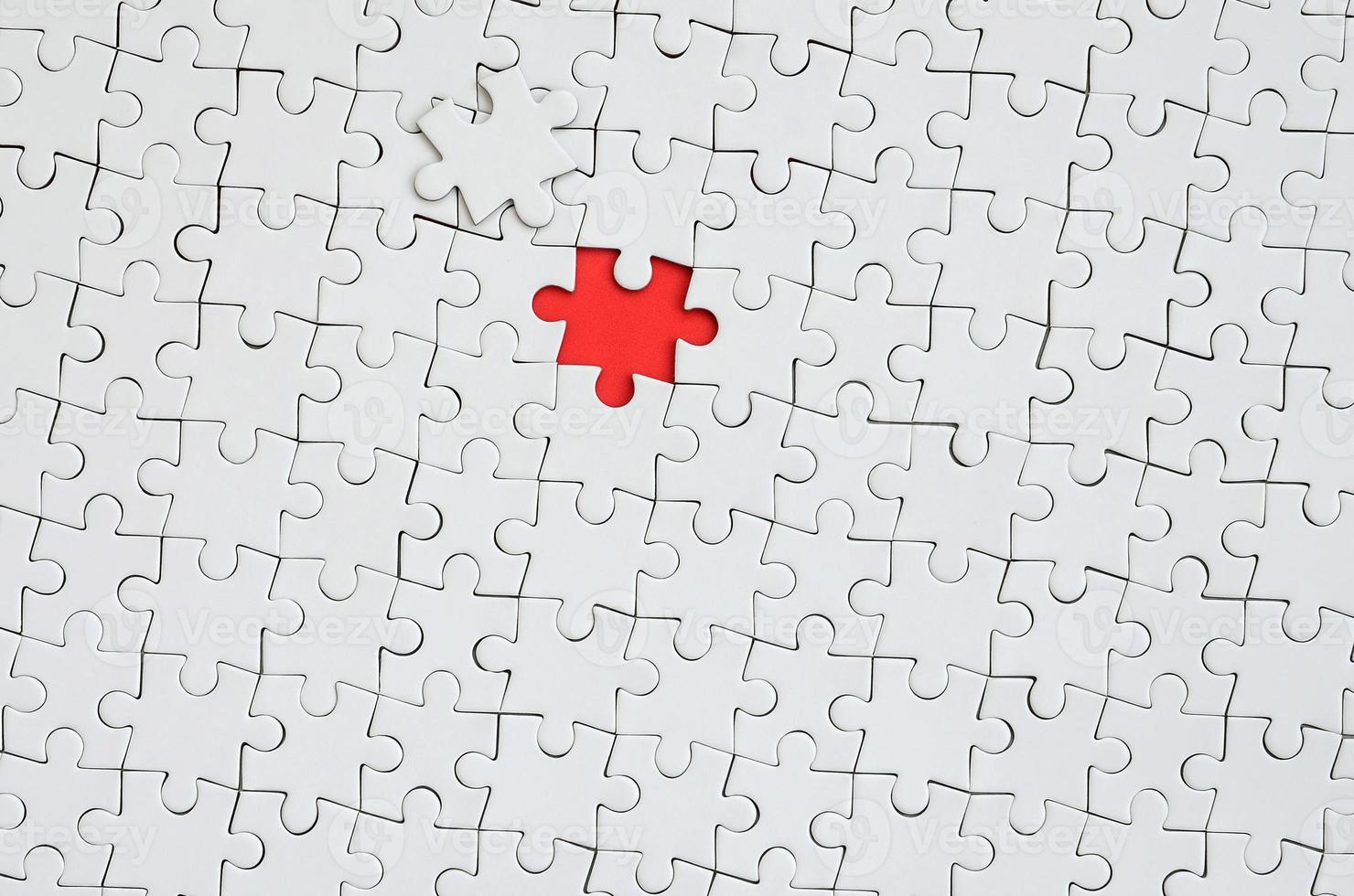 The texture of a white jigsaw puzzle in an assembled state with one missing element forming a red space photo