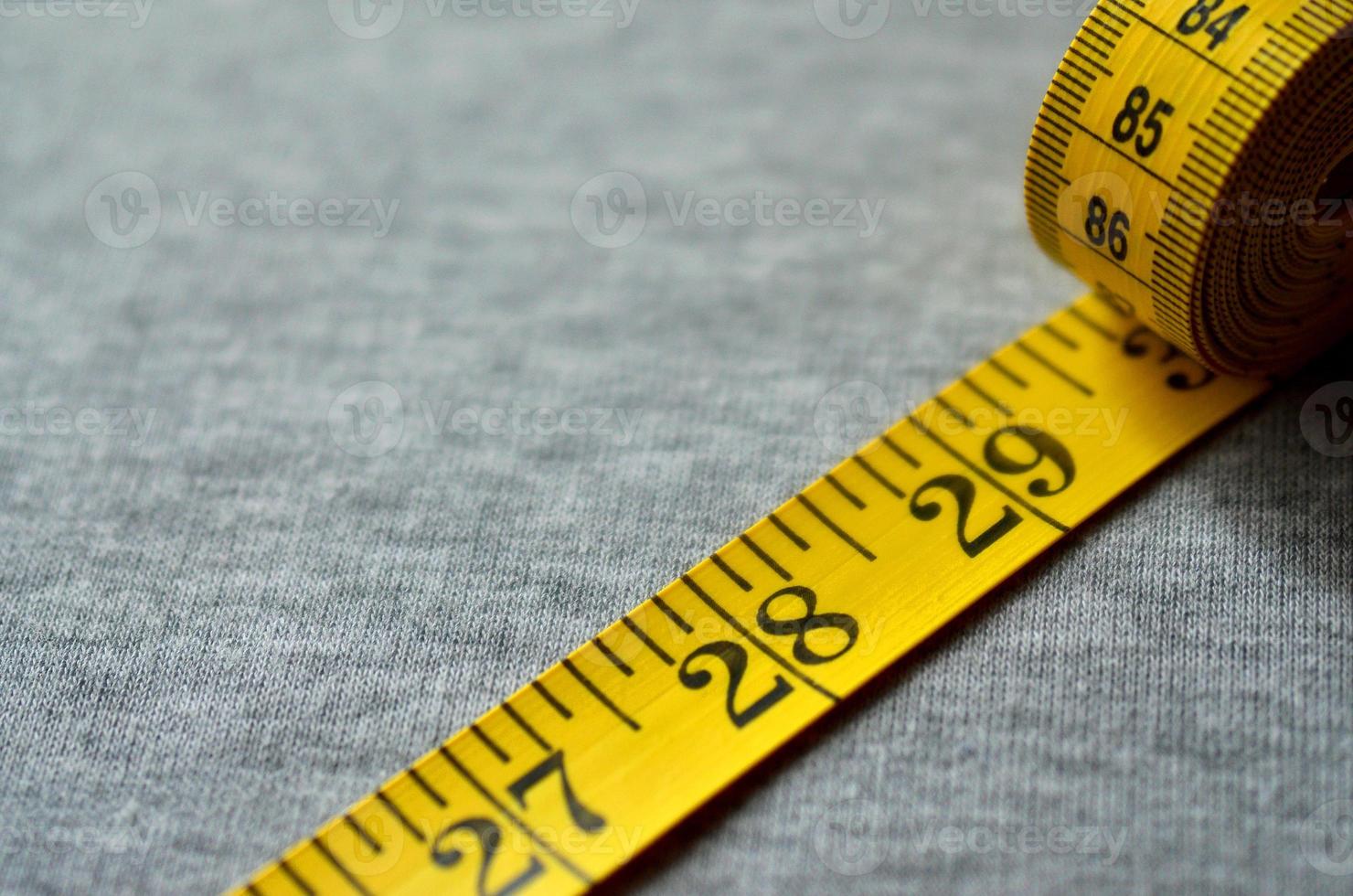 Yellow measuring tape lies on a gray knitted fabric photo