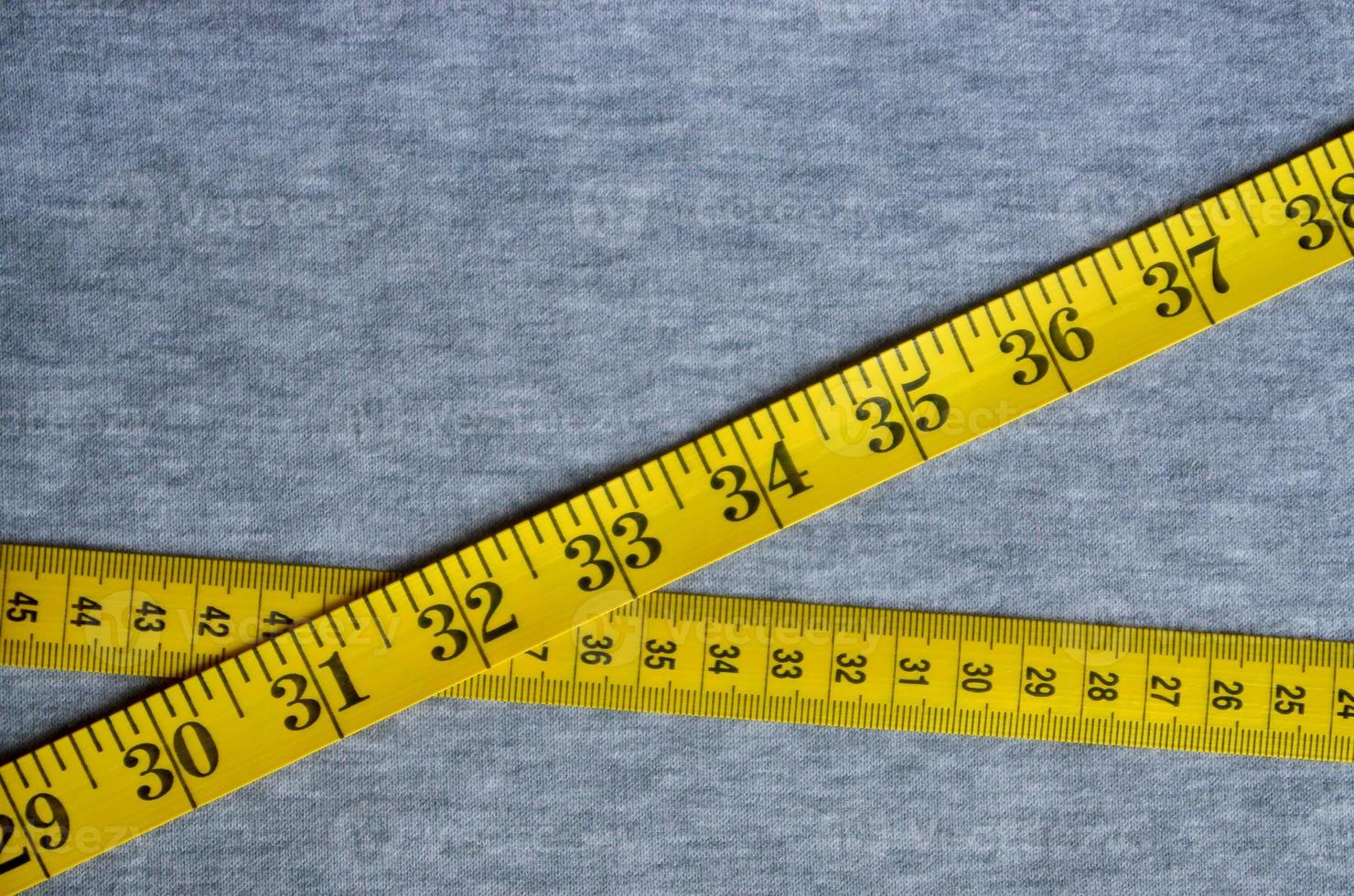 Yellow measuring tape lies on a gray knitted fabric photo