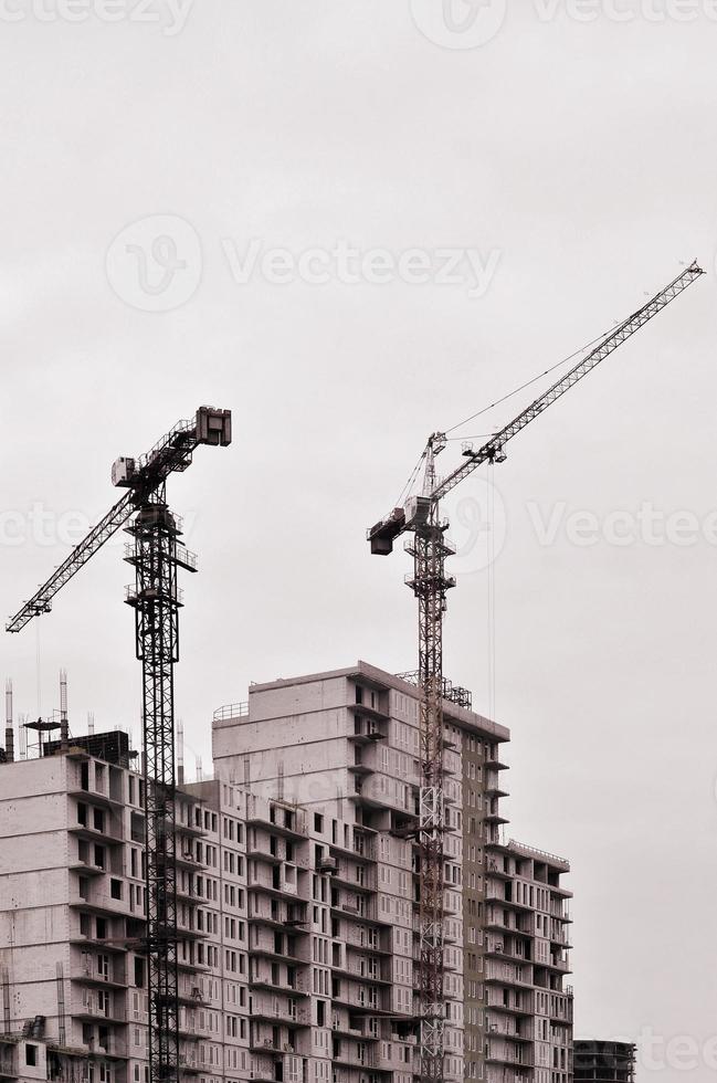 Working tall cranes inside place for with tall buildings under construction against a clear blue sky. Crane and building working progress. Retro tone photo