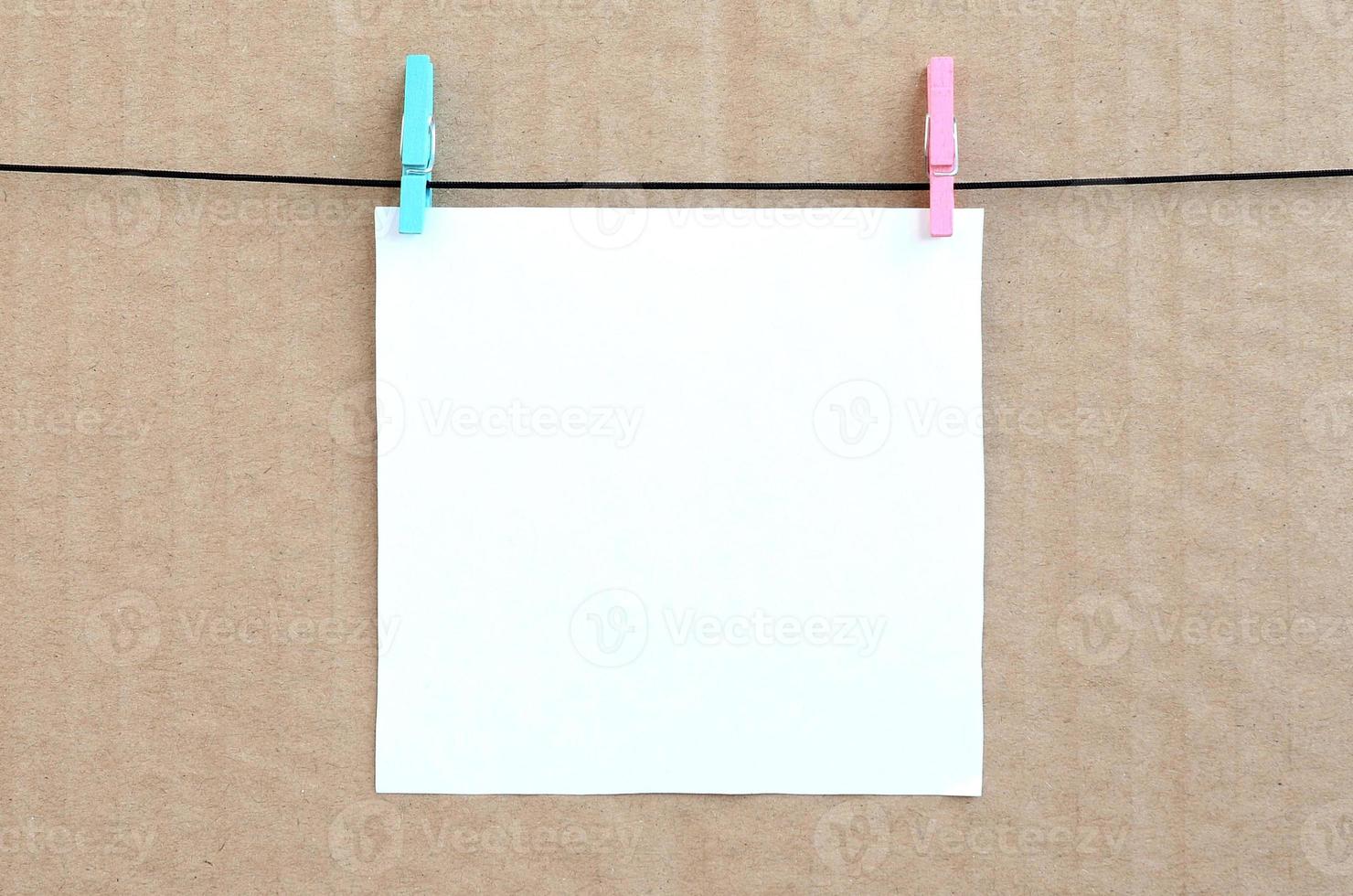 White blank card on rope on a brown cardboard background. Creative reminder, small sheet of paper on wooden clothespin, memo backdrop photo