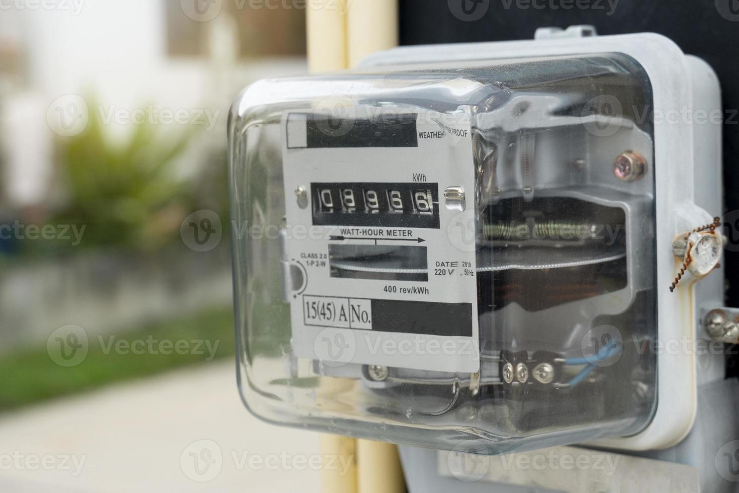 Power meter of Thailand attached to outdoor power pole. Blurred image of a fence next to a house covered with green grass. photo