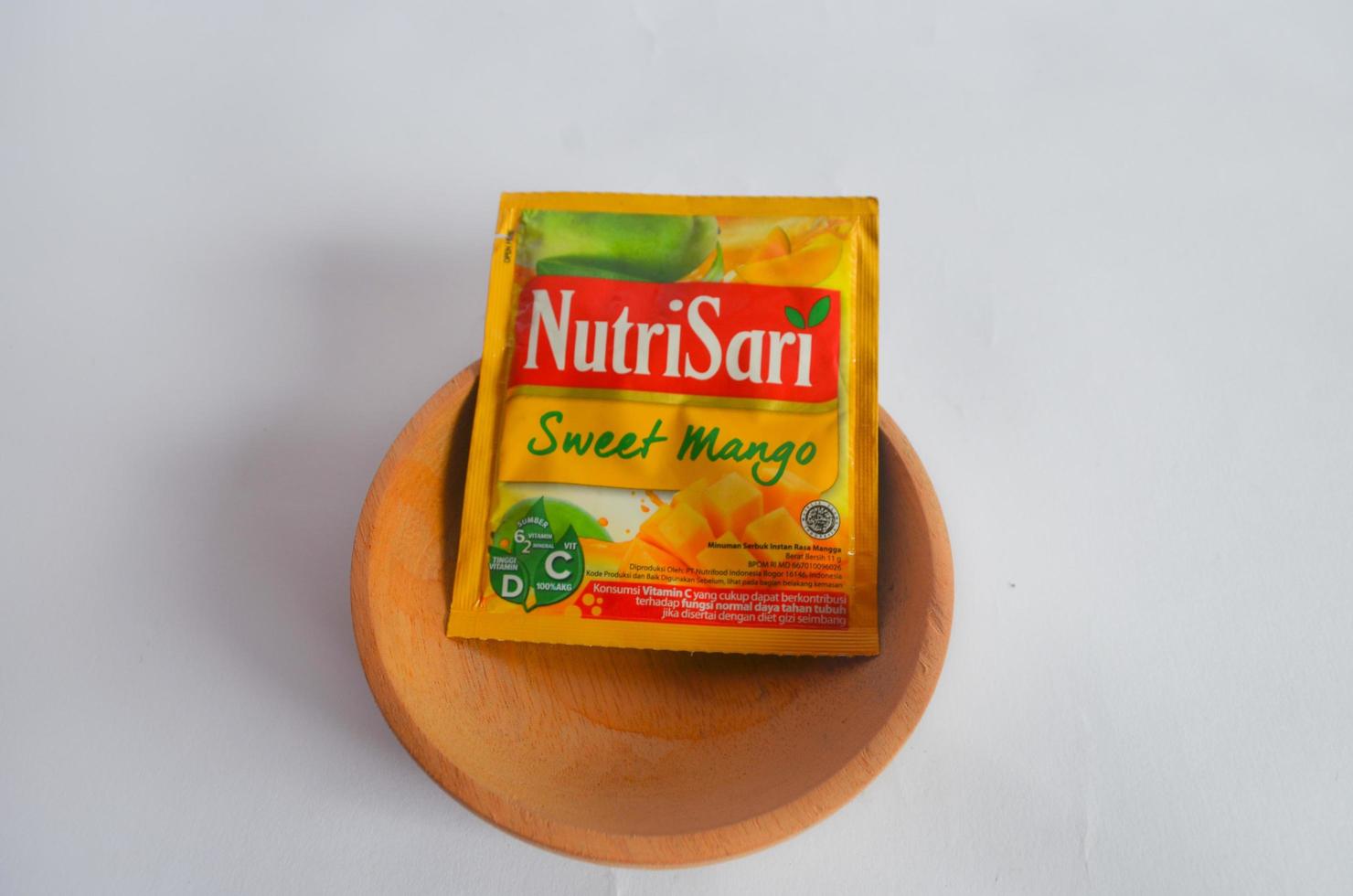 BLITAR, INDONESIA - October 9, 2022 Nutrisari, a popular powdered juice drink in Indonesia, orange flavor in a wooden container isolated on a white background photo