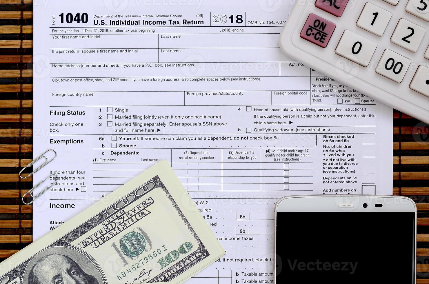 Composition of items lying on the 1040 tax form. Dollar bills, calculator, smartphone, paper clip and notepad. The time to pay taxes photo