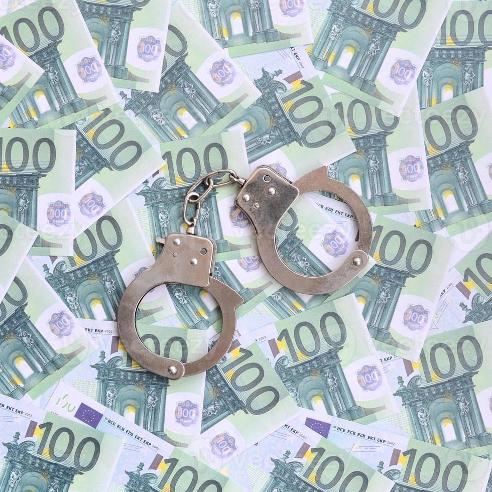 Police handcuffs lies on a set of green monetary denominations of 100 euros. A lot of money forms an infinite heap photo