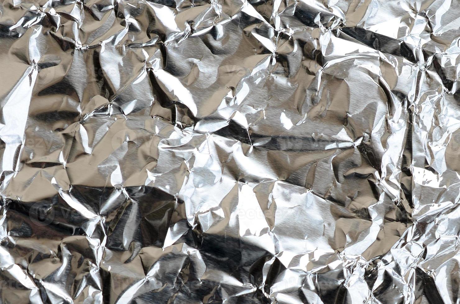 Thin wrinkled sheet of crushed tin aluminum silver foil background with shiny crumpled surface for texture photo