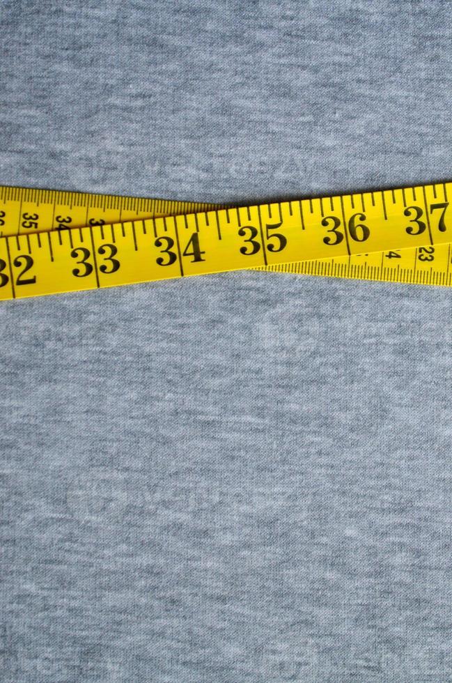 Yellow measuring tape lies on a gray knitted fabric photo