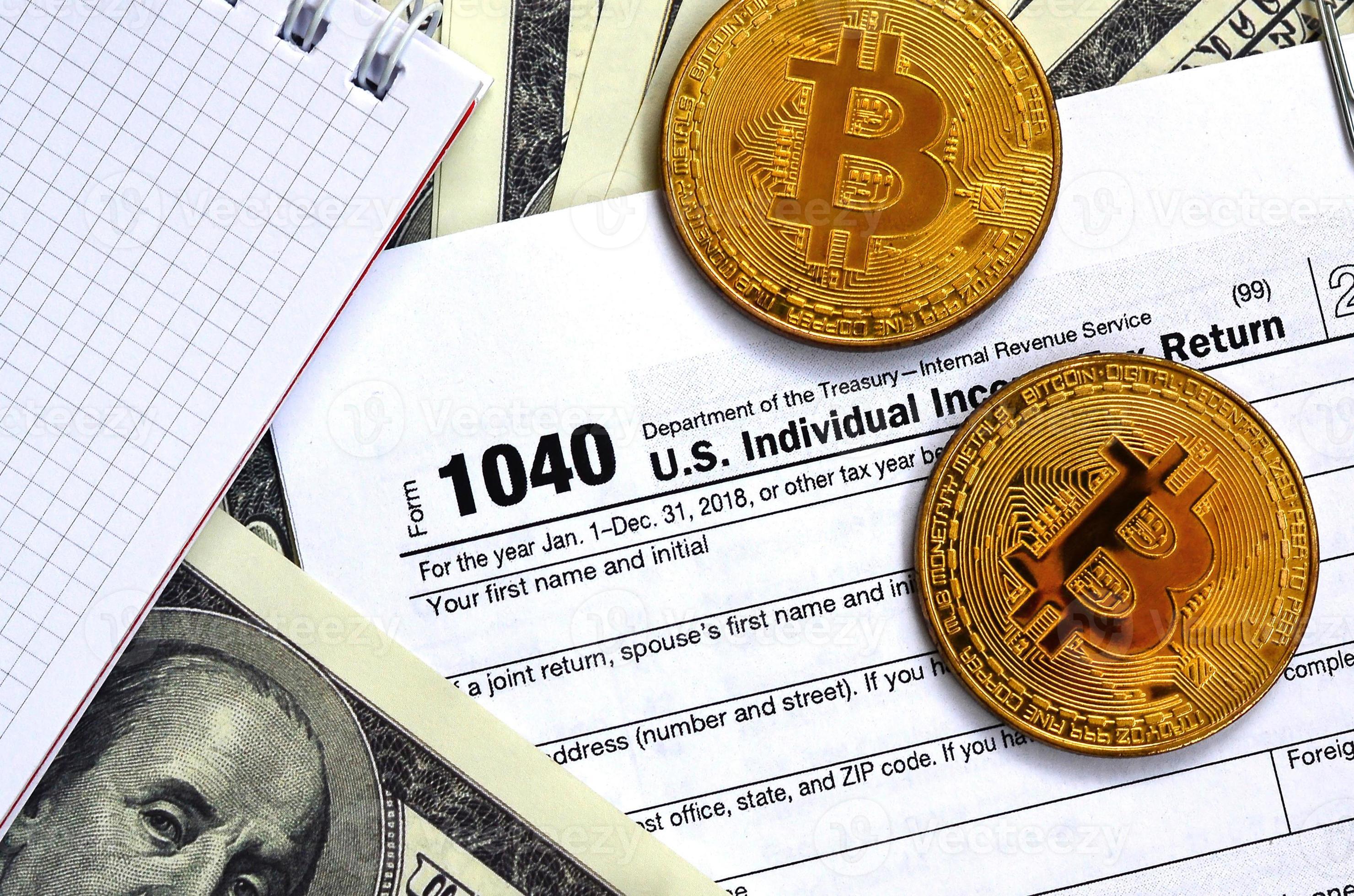 The pen, bitcoins and dollar bills is lies on the tax form 1040 U.S