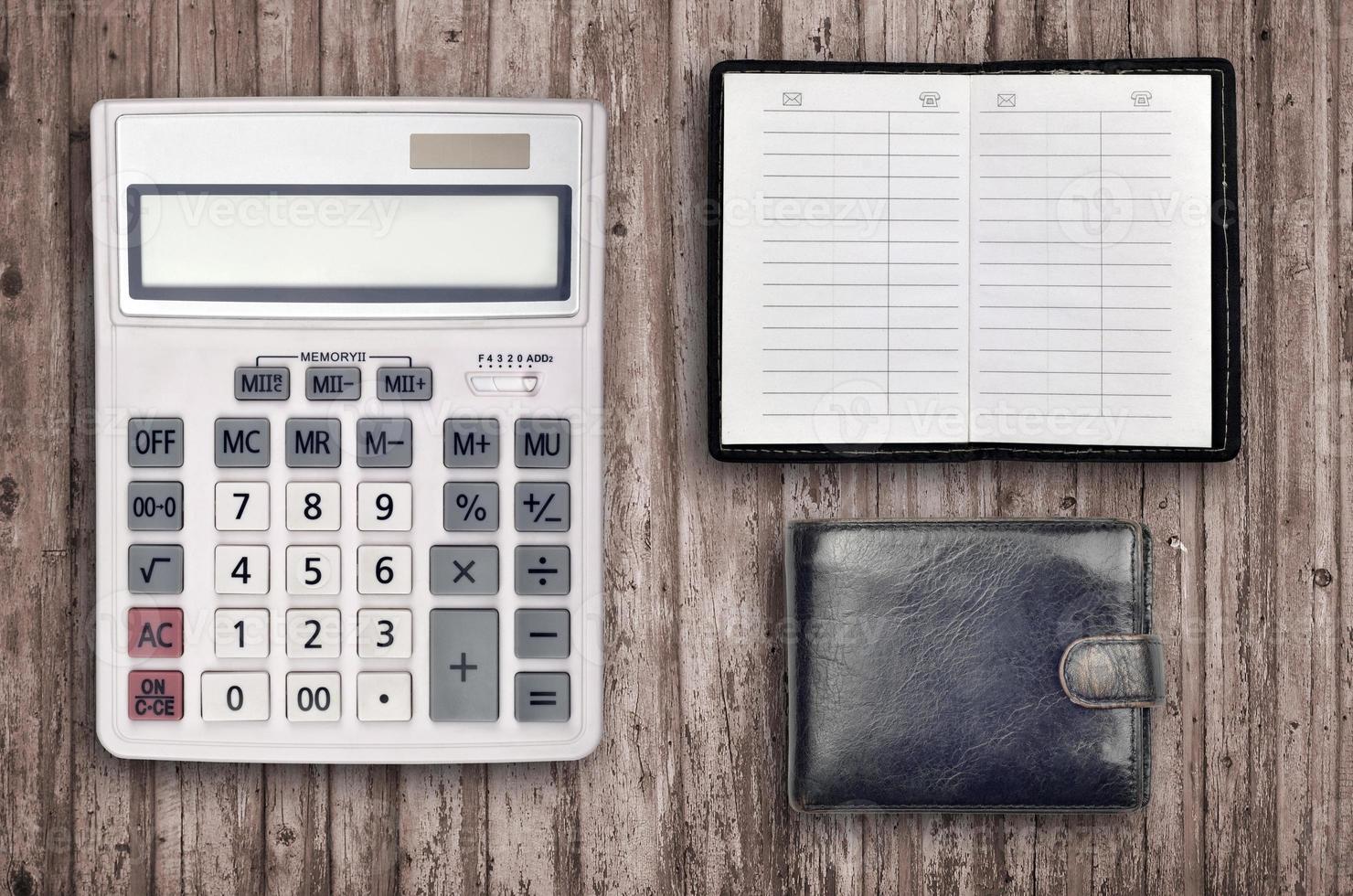 Office flat lay composition with calculator, address book and black purse on brown wooden table background with top view. Accountant paperwork concept photo