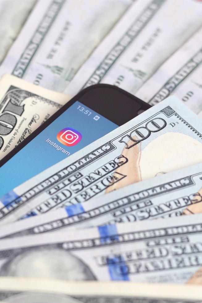 KHARKOV, UKRAINE - JULY 2, 2021 Smartphone screen with Instagram app and lot of hundred dollar bills. Business and social networking concept photo