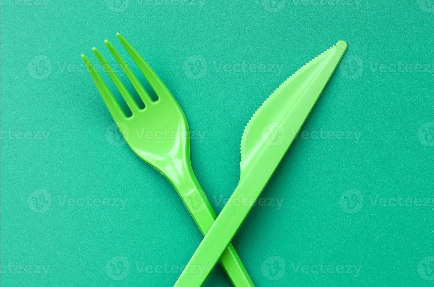 Disposable plastic cutlery green. Plastic fork and knife lie on a green background surface photo