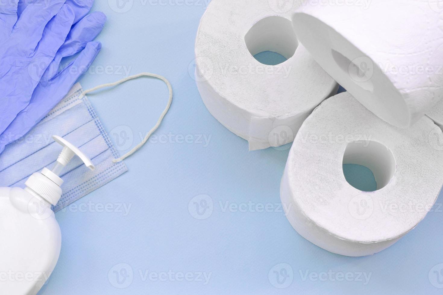 Set of important items for Covid-19 quarantine times. Toilet paper, rubber disposable gloves with surgical face mask and liquid soap bottle on blue background photo