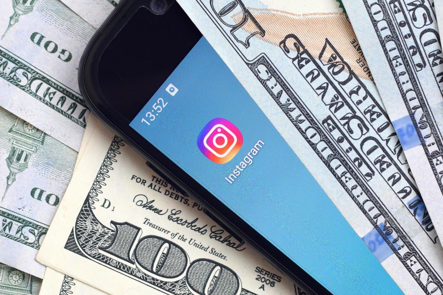 KHARKIV, UKRAINE - MAY 4, 2020 Smartphone screen with Instagram app and lot of hundred dollar bills. Business and social networking concept photo