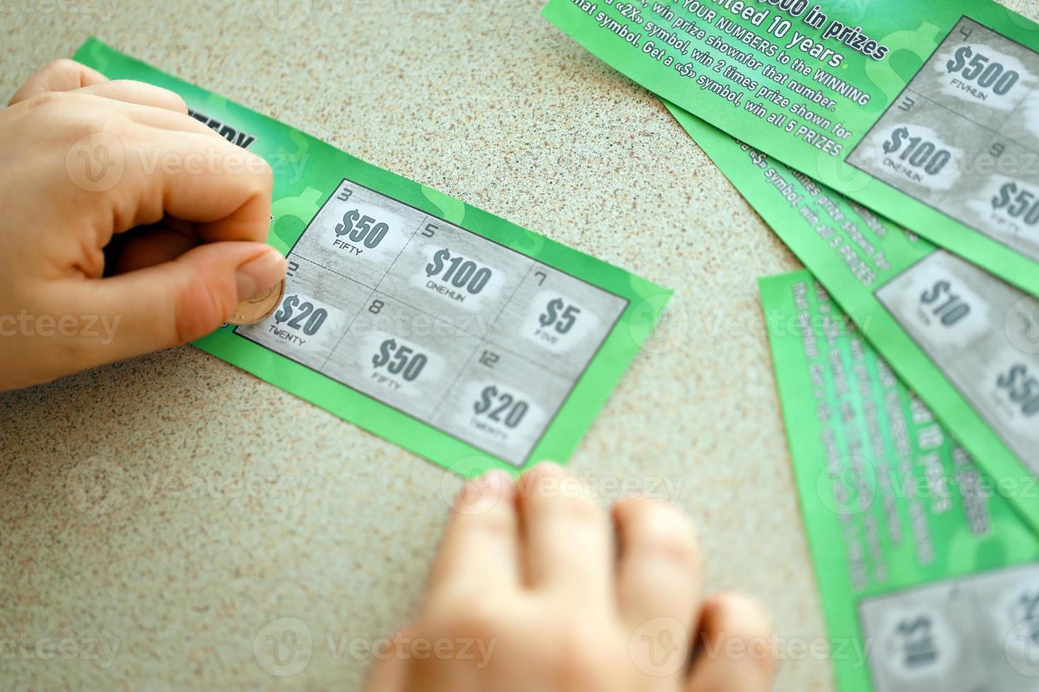 Close up view of silver coin in hand of gambler scratching fake lottery card. Lottery gambling concept, scratching cards lottery photo