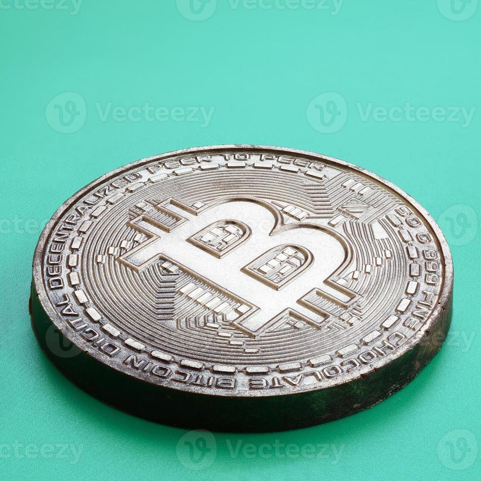 Chocolate product in the form of physical bitcoin lies on a green plastic background. Model of the crypto currency in the edible form photo
