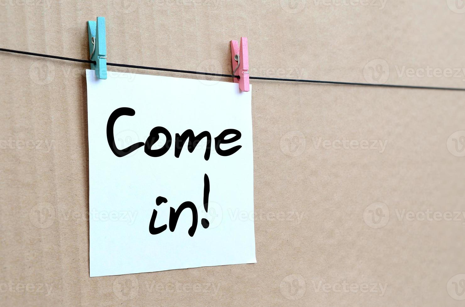 Come in Note is written on a white sticker that hangs with a clothespin on a rope on a background of brown cardboard photo