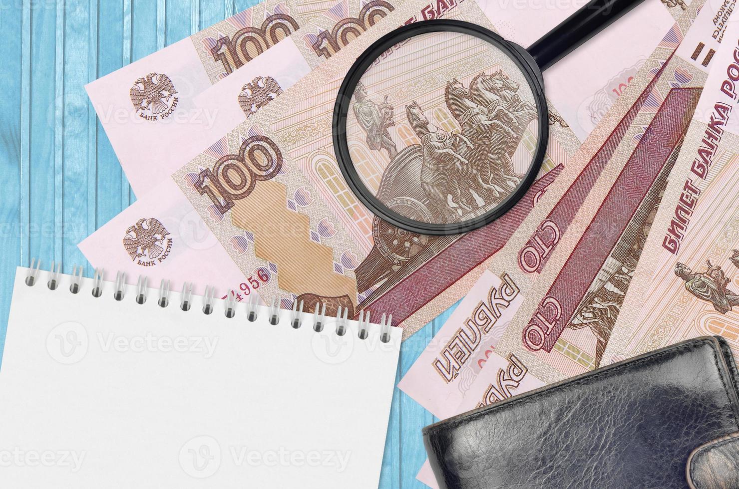 100 russian rubles bills and magnifying glass with black purse and notepad. Concept of counterfeit money. Search for differences in details on money bills to detect fake photo