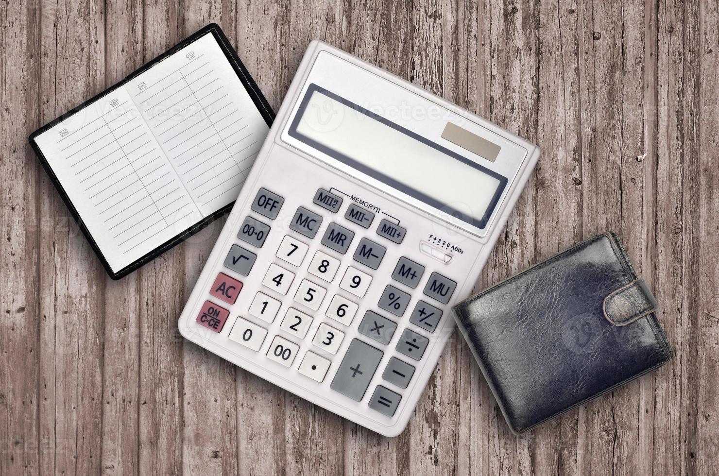 Office flat lay composition with calculator, address book and black purse on brown wooden table background with top view. Accountant paperwork concept photo