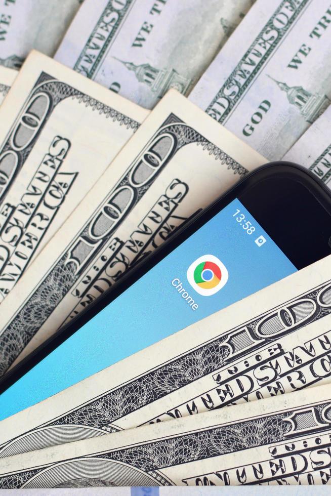 KHARKOV, UKRAINE - JULY 2, 2021 Smartphone screen with Google chrome app and lot of hundred dollar bills. Business and social networking concept photo