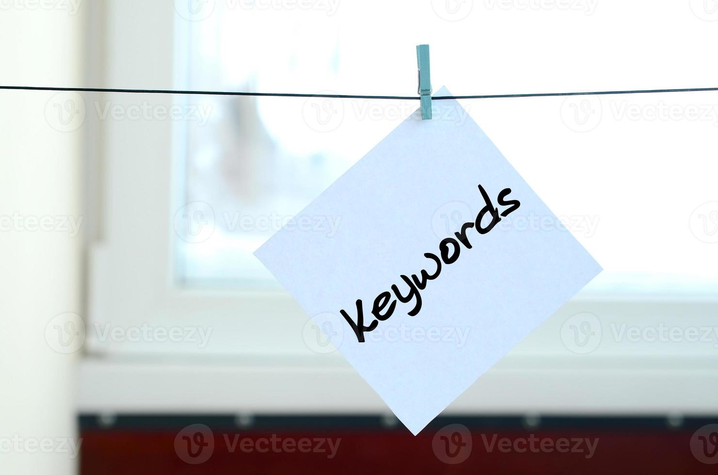 Keywords. Note is written on a white sticker that hangs with a clothespin on a rope on a background of window glass photo