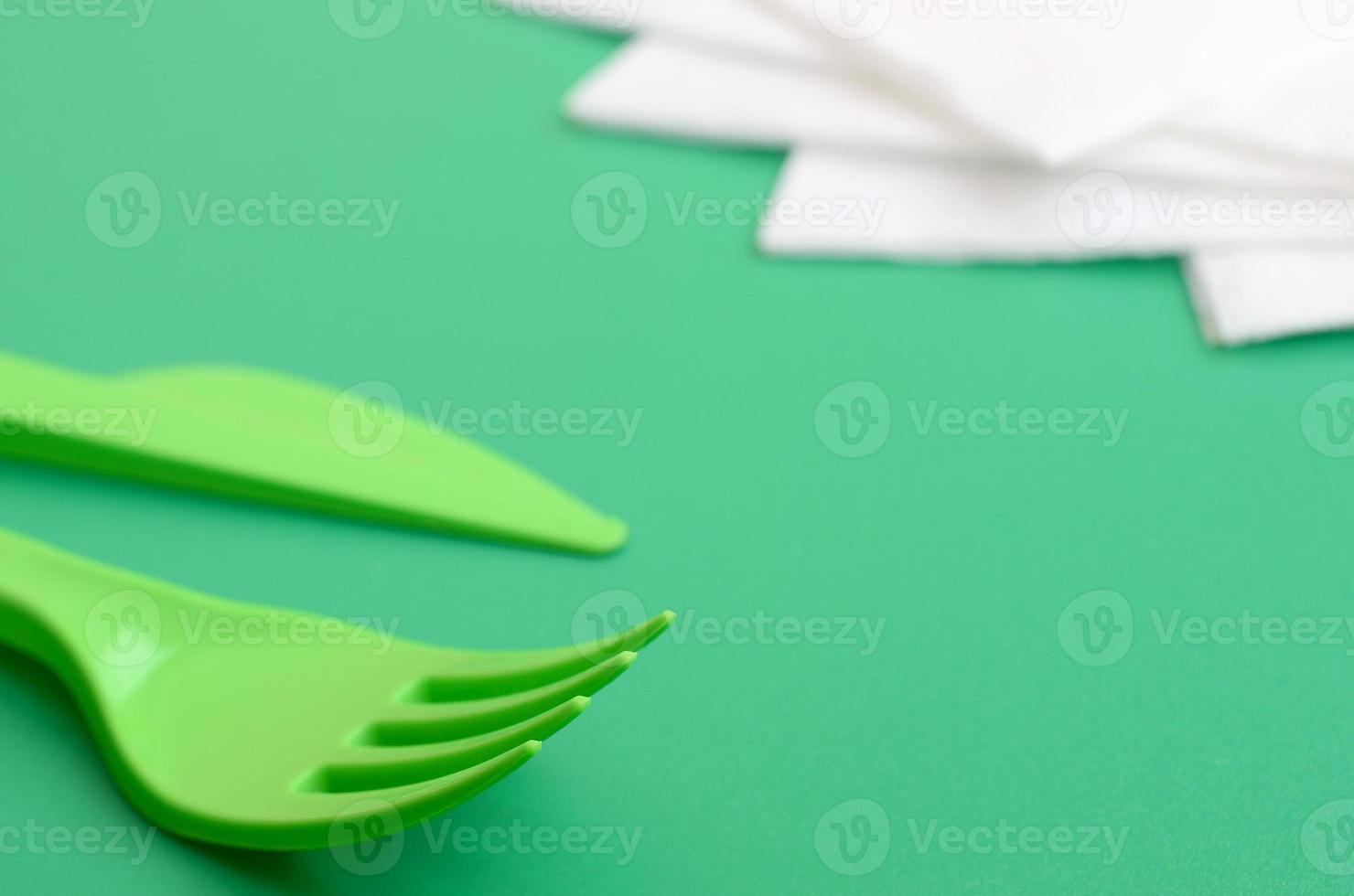 Disposable plastic cutlery green. Plastic fork and knife lie on a green background surface next to napkins photo