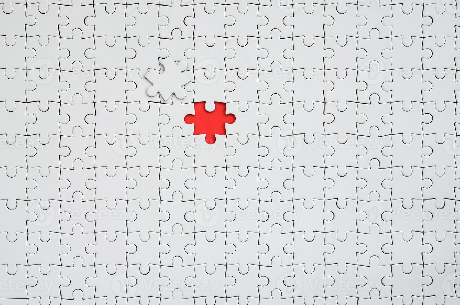 The texture of a white jigsaw puzzle in an assembled state with one missing element forming a red space photo