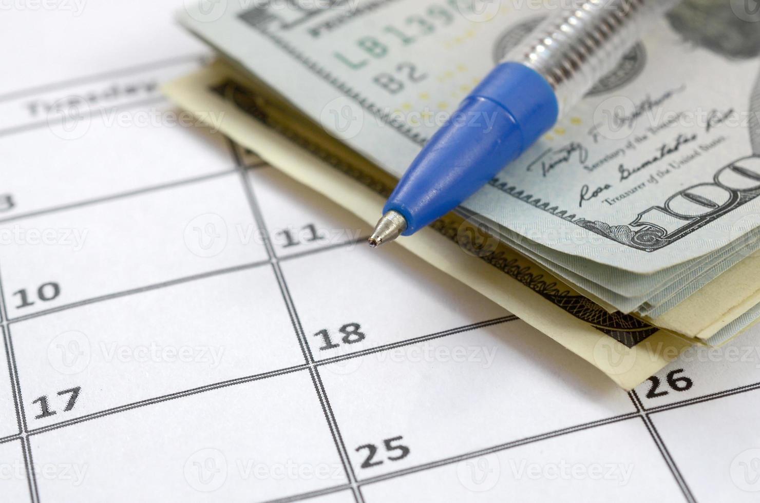 Pen and many hundred US dollar bills on calendar page close up photo