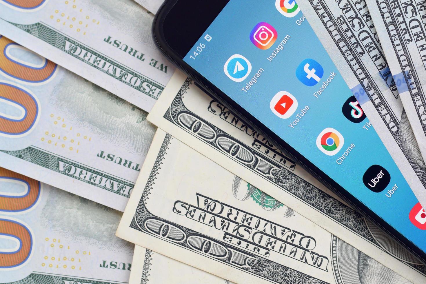 KHARKOV, UKRAINE - JULY 2, 2021 Smartphone screen with many popular apps and lot of hundred dollar bills. Business and social networking concept photo