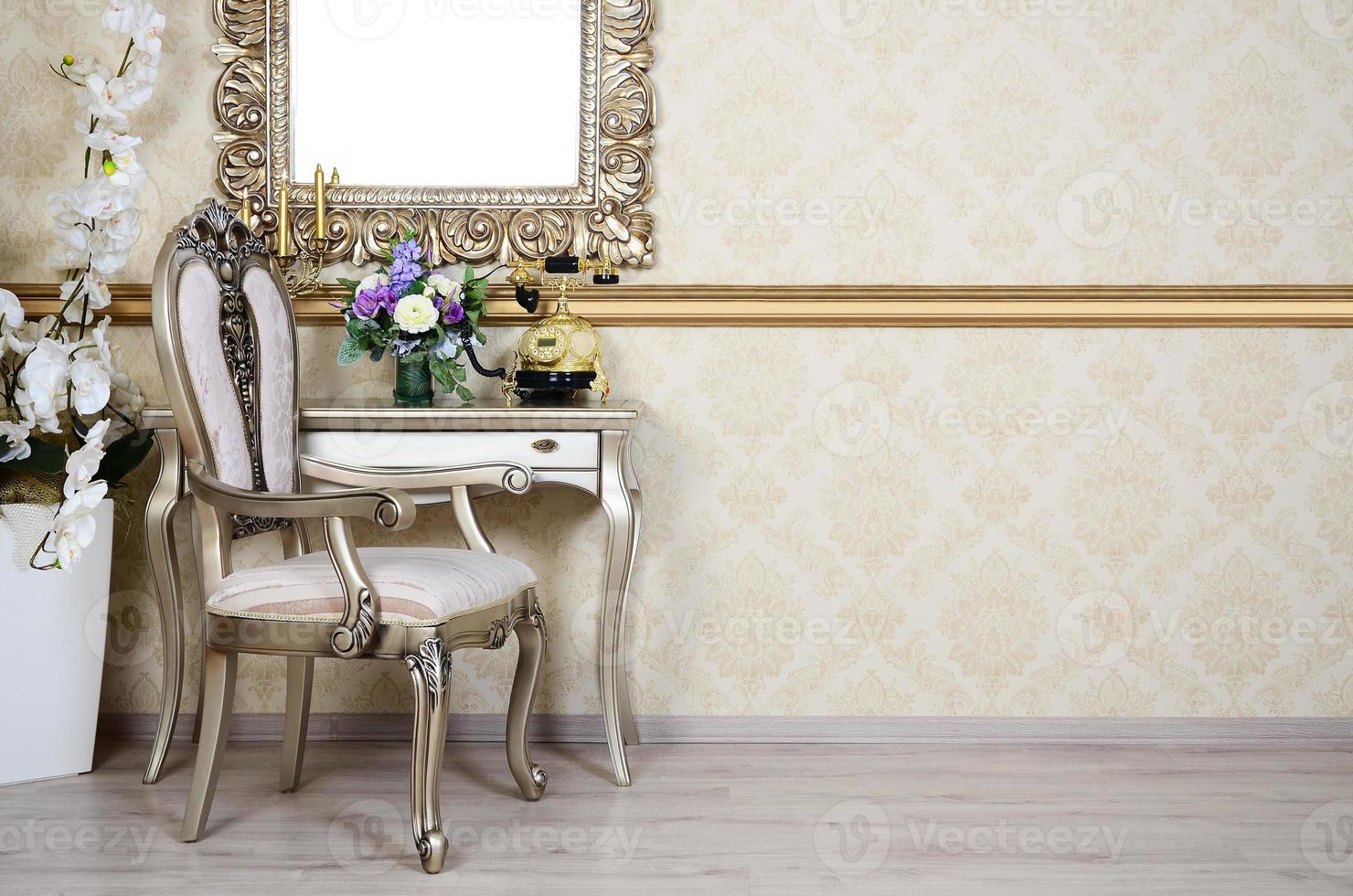 A fragment of a retro interior with a chair and table, on which is a telephone and a vase of flowers. Above the table hangs an empty picture frame for your photo