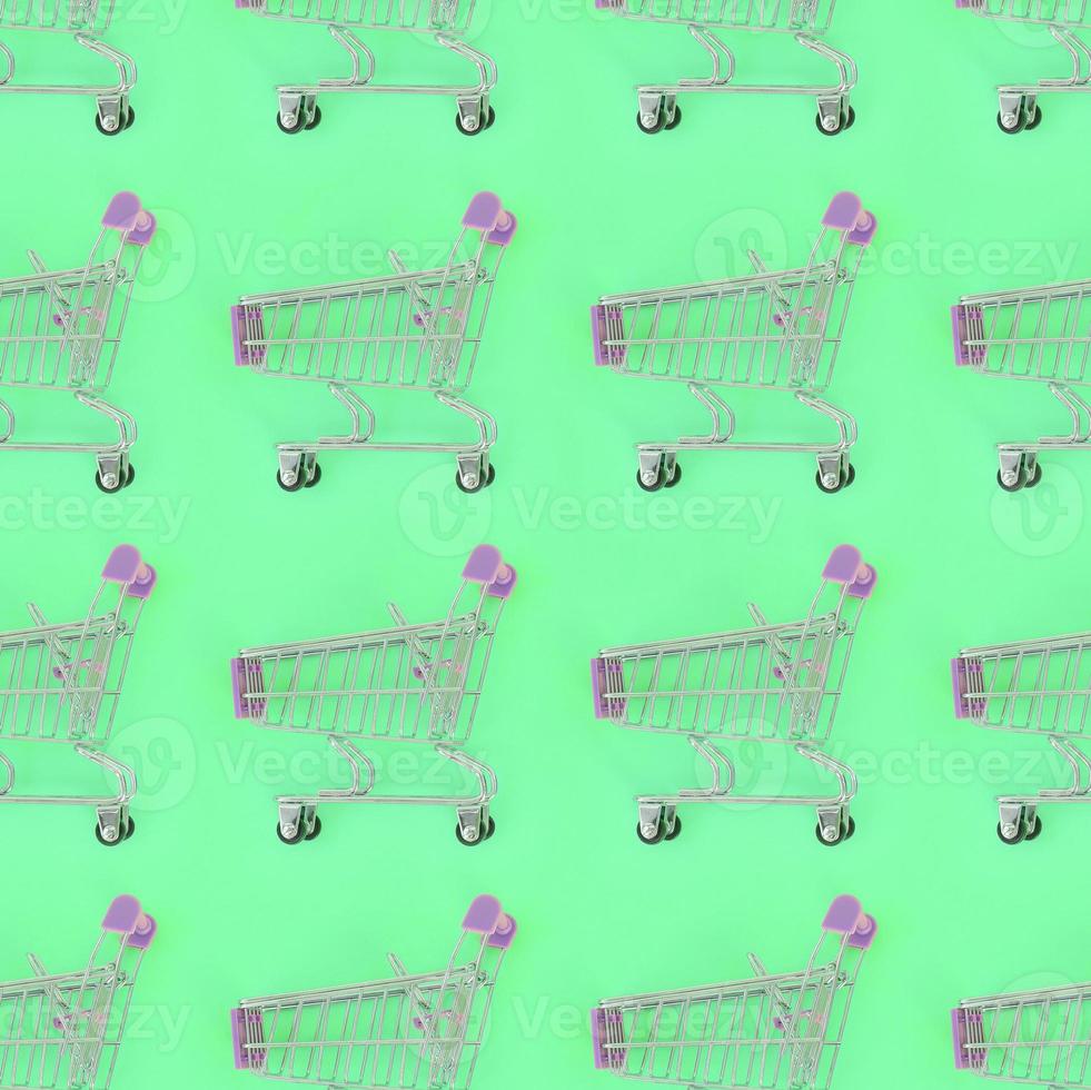 Shopping addiction, shopping lover or shopaholic concept. Many small empty shopping carts perform a pattern on a pastel colored paper background. Flat lay composition, top view photo