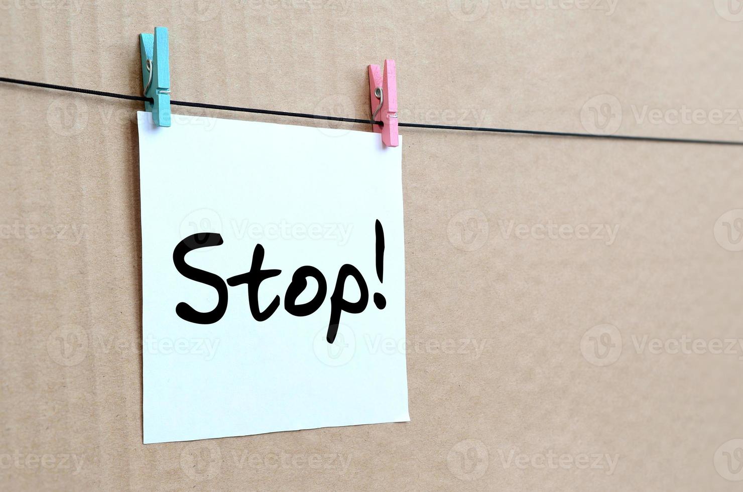 Stop Note is written on a white sticker that hangs with a clothespin on a rope on a background of brown cardboard photo