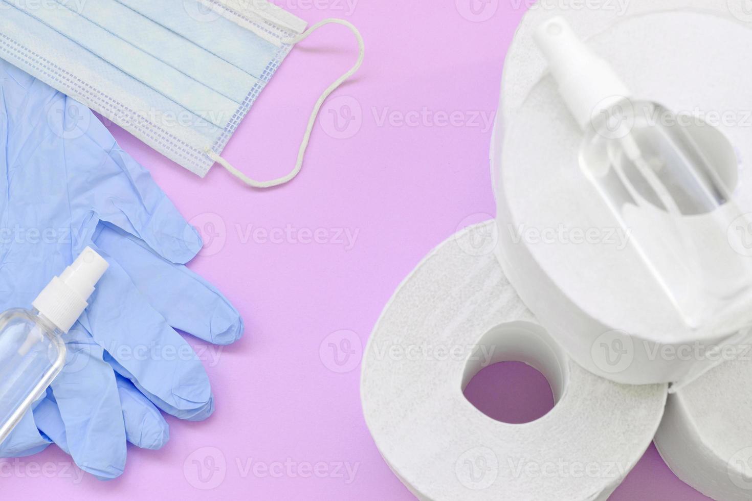 Set of important items for Covid-19 quarantine. Toilet paper, rubber disposable gloves with surgical face mask and hand sanitizer on lilac background photo